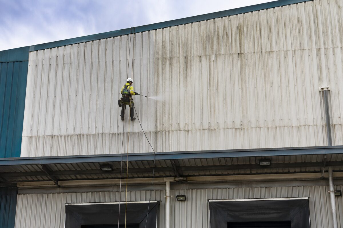 Rope-access technician pressure washing high-level industrial cladding